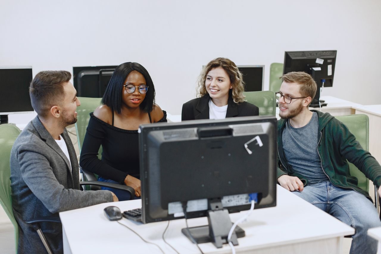 A diverse group of colleagues collaborating on a project around a computer in an office.